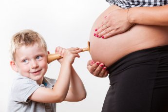 Sohn lauscht mit Stethoskop am Schwangerschaftsbauch der Mama