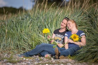 Zwei Schwestern liegen in hohem Gras und halten eine Sonnenblume in der Hand