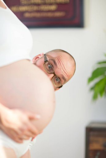 Witziges Fotos vom Schwangerschaftsshooting: Mann guckt hinter dem Babybauch der Mama hervor