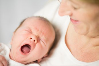 Von oben fotografiert: Das Baby liegt gähnend im Arm der Mama