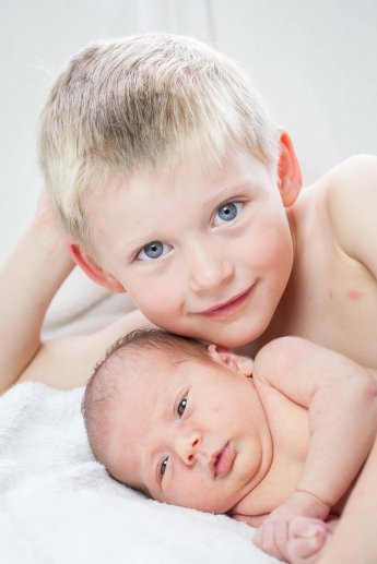 Die blauen Augen des großen bruders blicken in die Kamera während unter ihm seine kleine Baby-Schwester liegt
