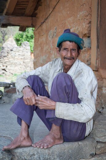 Indischer Bauer hockt vor einem ärmlichen Bauernhaus