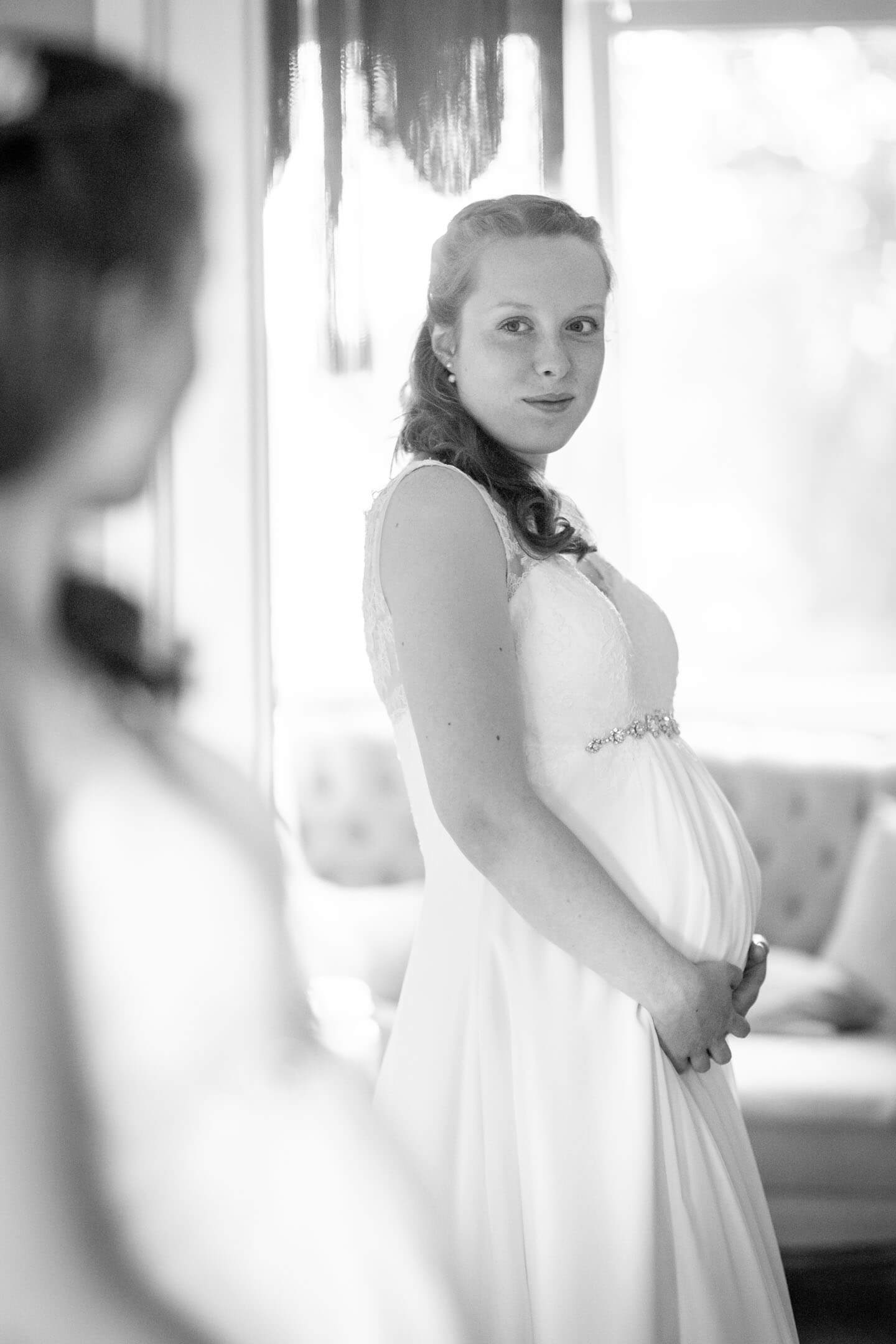 Schwangere Braut betrachtet sich im Spiegel.