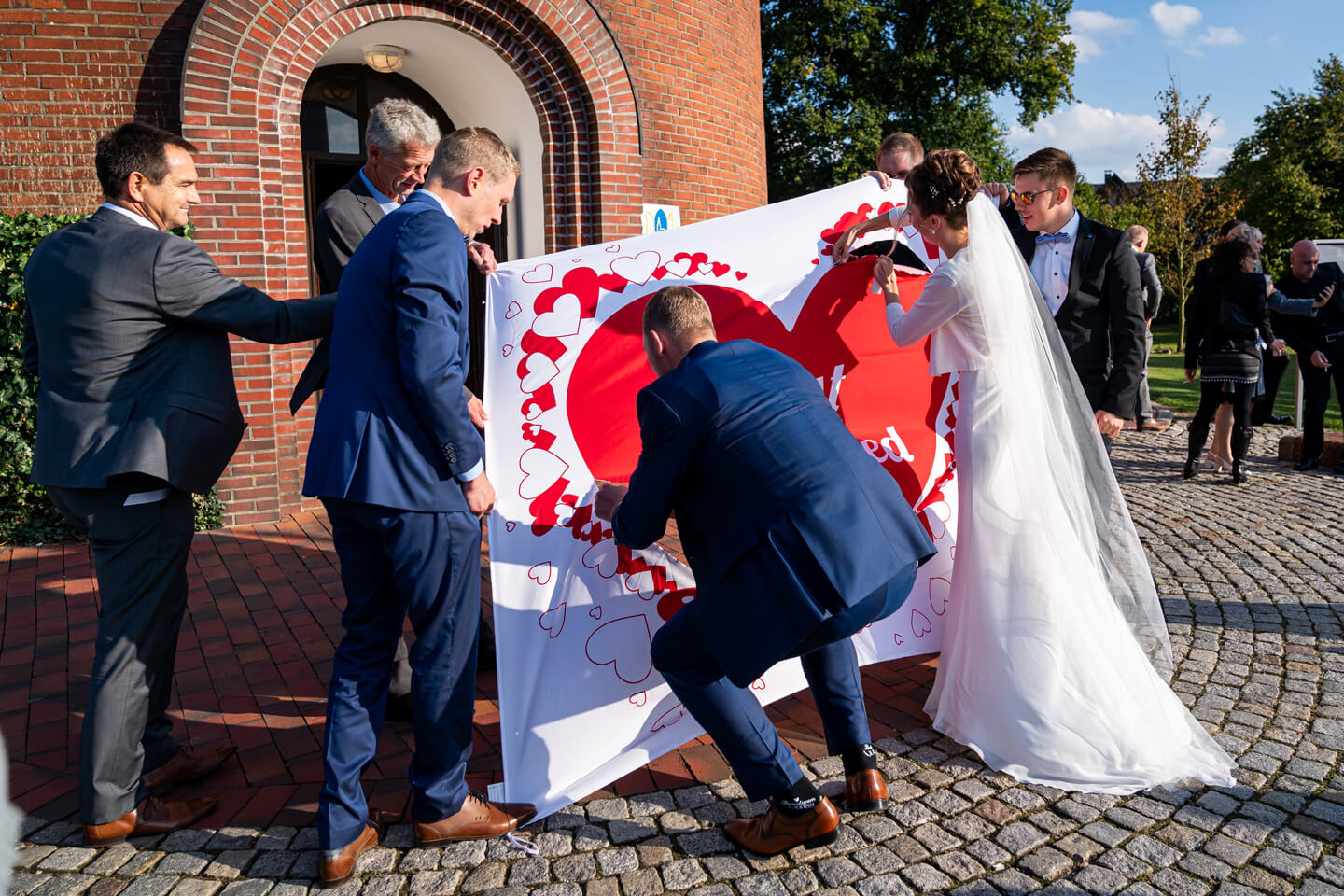 Hochzeitspaar schneidet vor der Kirchentür ein Herz aus einem Bettlaken