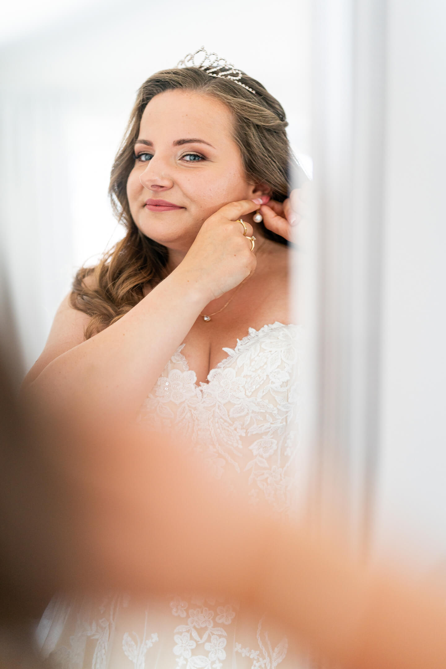 Braut steckt sich Ohrringe vor dem Spiegel an.