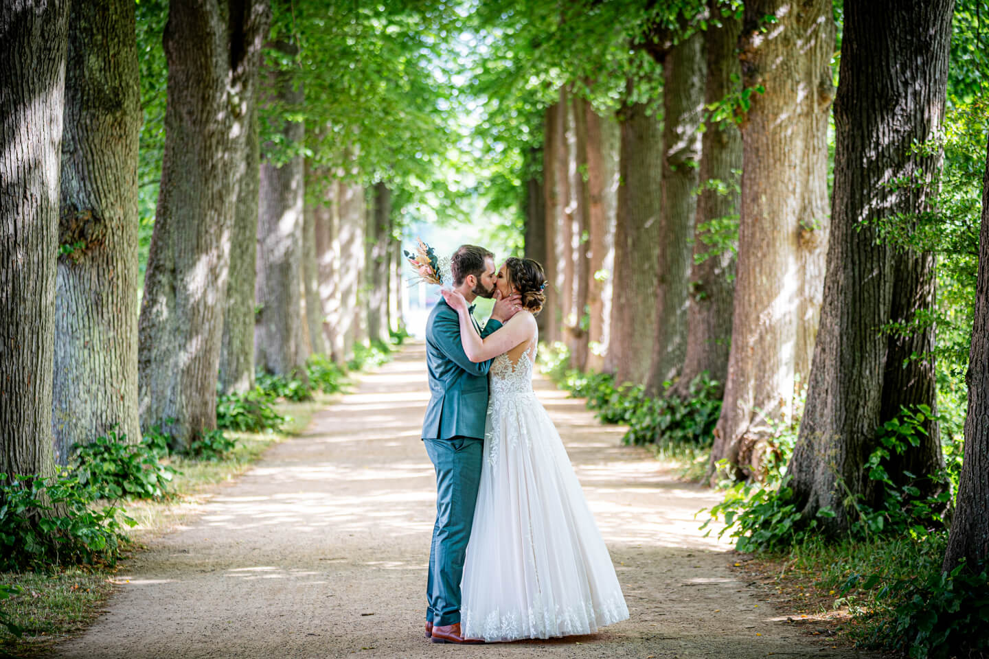 Brautpaar küsst sich in der Baumallee hinter dem Schloss Eutin.