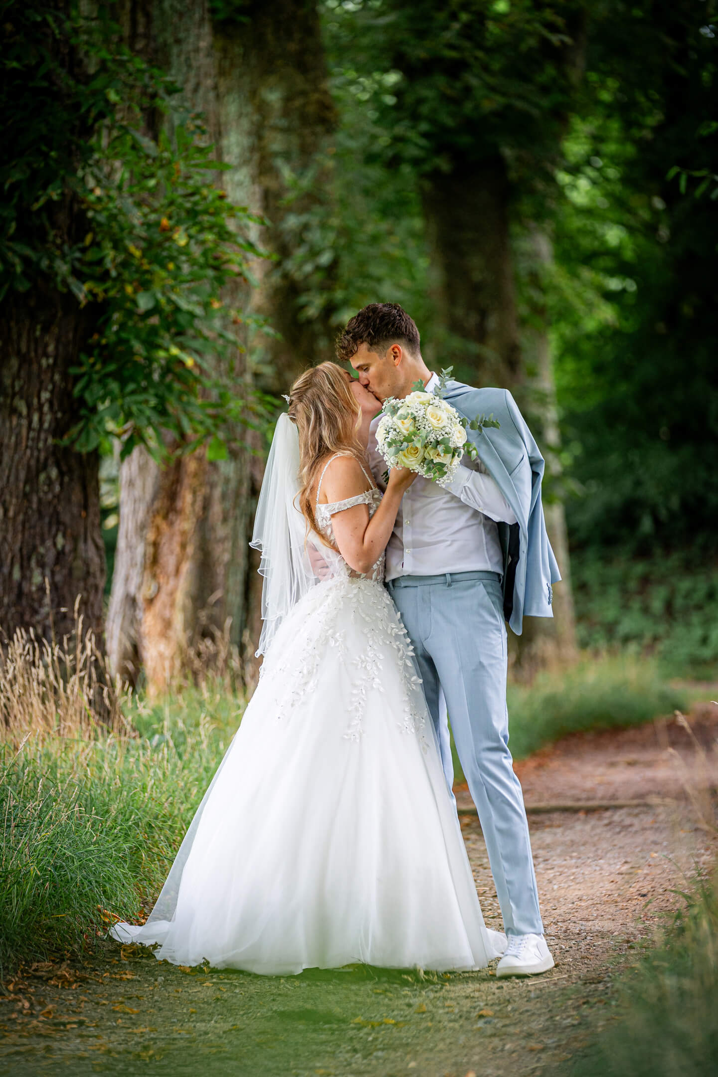Hochzeitspaar küsst sich in einer Kastanienallee.